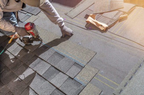 Roofing contractor installing asphalt shingles with a nail gun on a sloped roof.