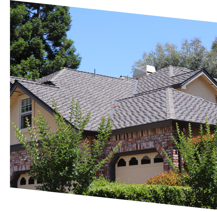 Brick-front suburban home with gray asphalt shingle roof and attached garage, surrounded by trees and landscaping.