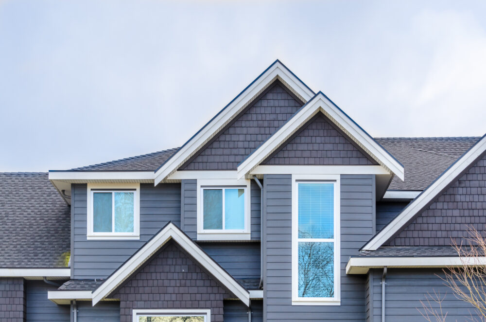 Gray house exterior with multiple gables and blue-tinted windows beneath a gray shingle roof.
