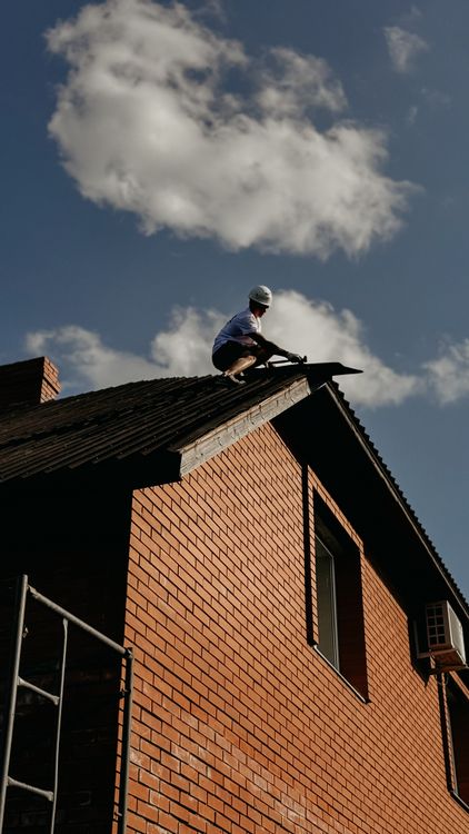 Professional roofing contractor in protective gear inspecting and repairing a roof